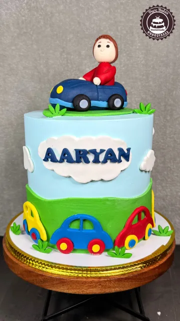 Colorful car themed birthday cake for Aaryan featuring playful edible cars and a child riding a blue car
