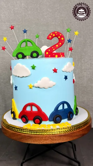 Colorful two year old birthday cake decorated with cars clouds stars and playful rainbow colors