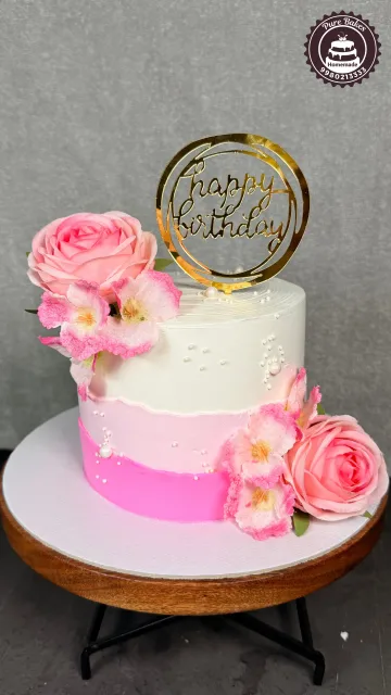 Elegant pink and white floral birthday cake decorated with roses, blossoms, pearls, and a gold Happy Birthday topper