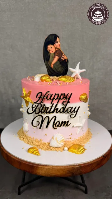 Pink birthday cake decorated with a mother and child topper, golden seashells, starfish, pearls, and beach-inspired details
